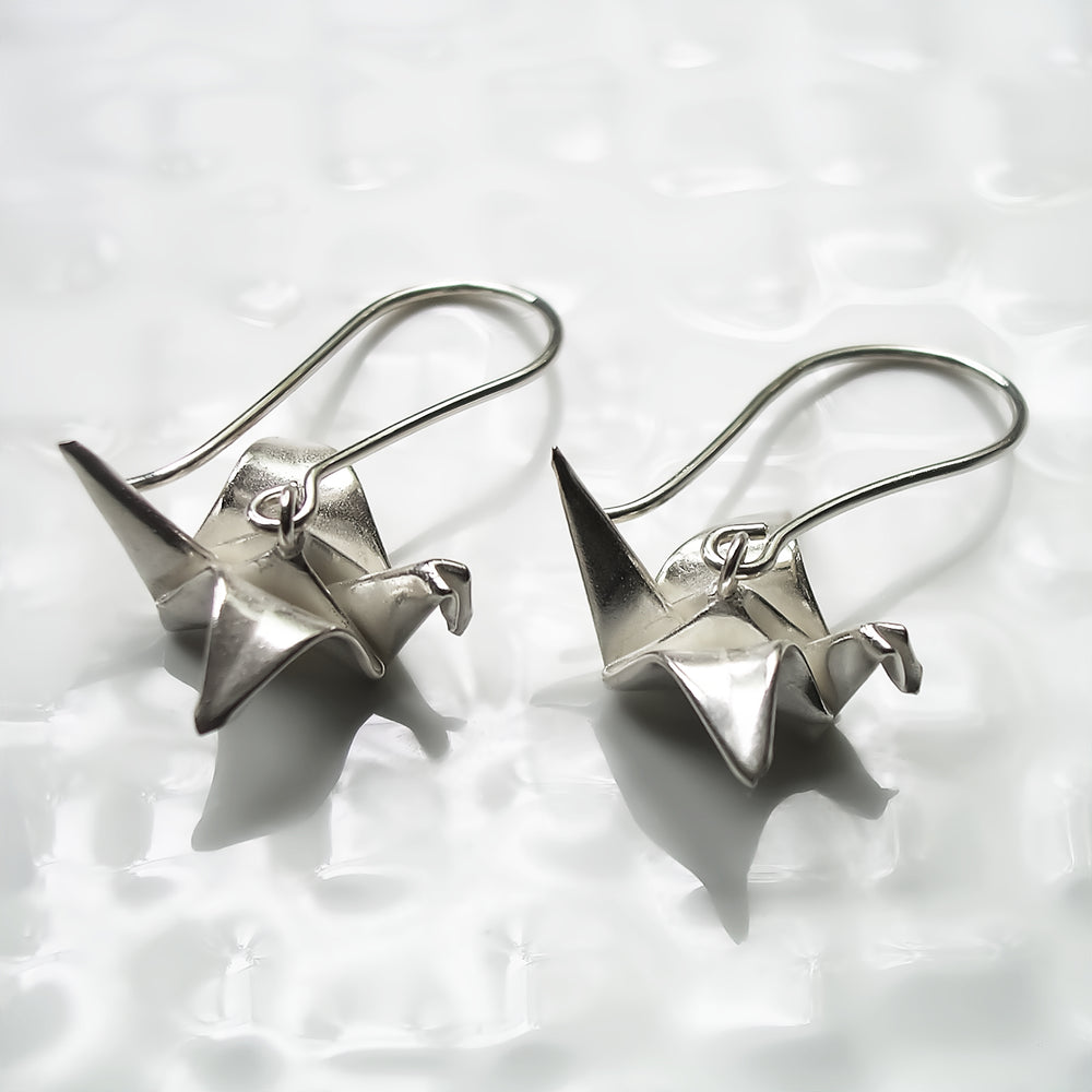 Bright silver origami peace crane earrings by Azulie, suspended from silver ear-wires