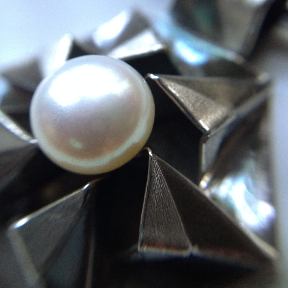 Fine silver origami pendant by Azulie, intricate hexagon design with a soft gunmetal patina, set with a Japanese creamy white pearl, on a black stainless steel multi-strand necklace, closeup view of pearl