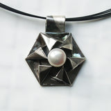 Fine silver origami pendant by Azulie, intricate hexagon design with a soft gunmetal patina, set with a Japanese creamy white pearl, on a black stainless steel multi-strand necklace