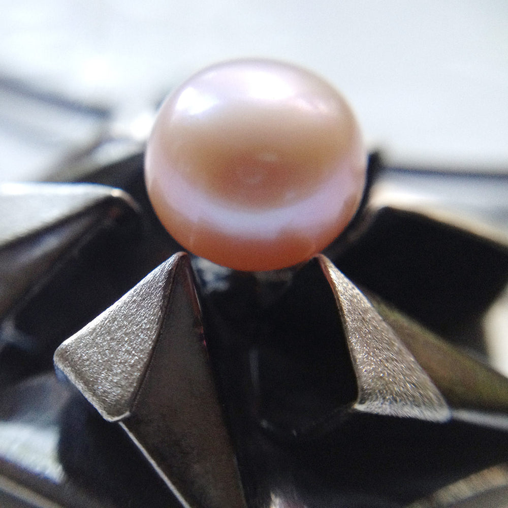 Fine silver origami pendant by Azulie, intricate hexagon design with a soft gunmetal patina, set with a Japanese pale pink pearl, on a black stainless steel multi-strand necklace, closeup view of pearl