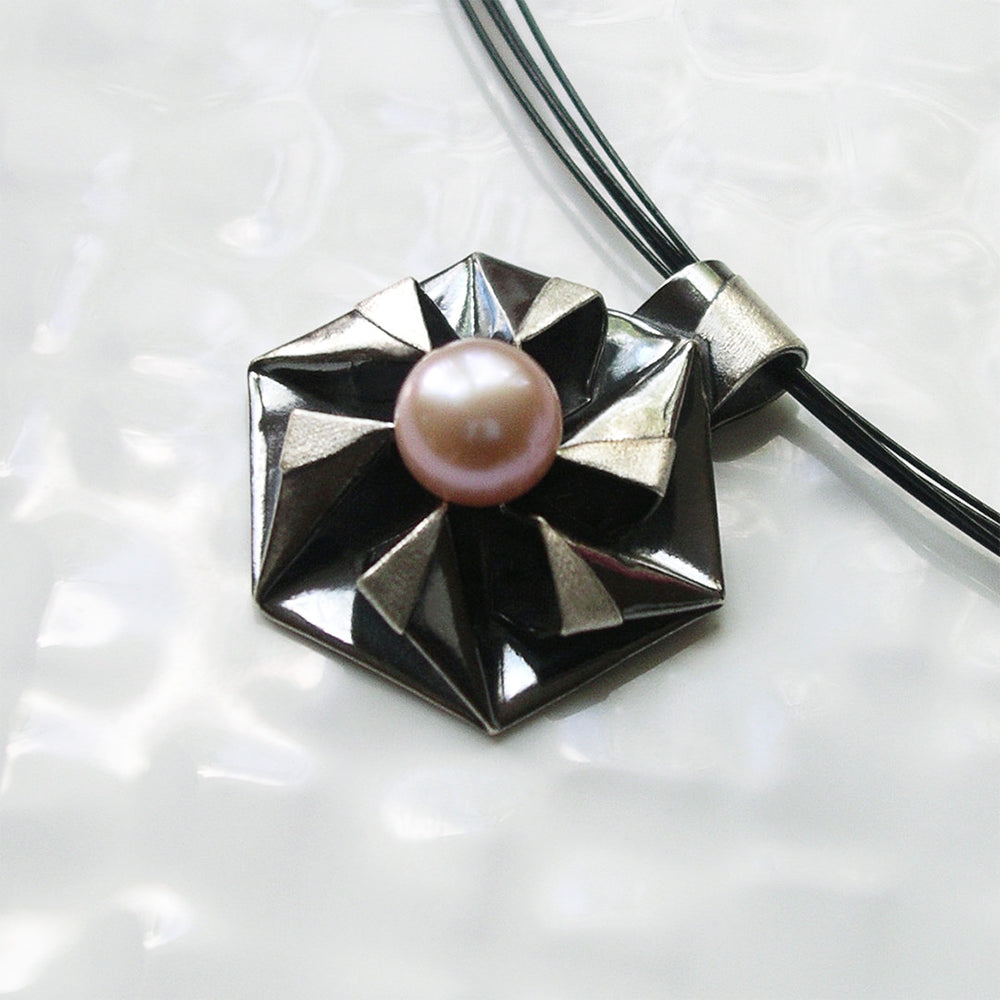 Fine silver origami pendant by Azulie, intricate hexagon design with a soft gunmetal patina, set with a Japanese pale pink pearl, on a black stainless steel multi-strand necklace